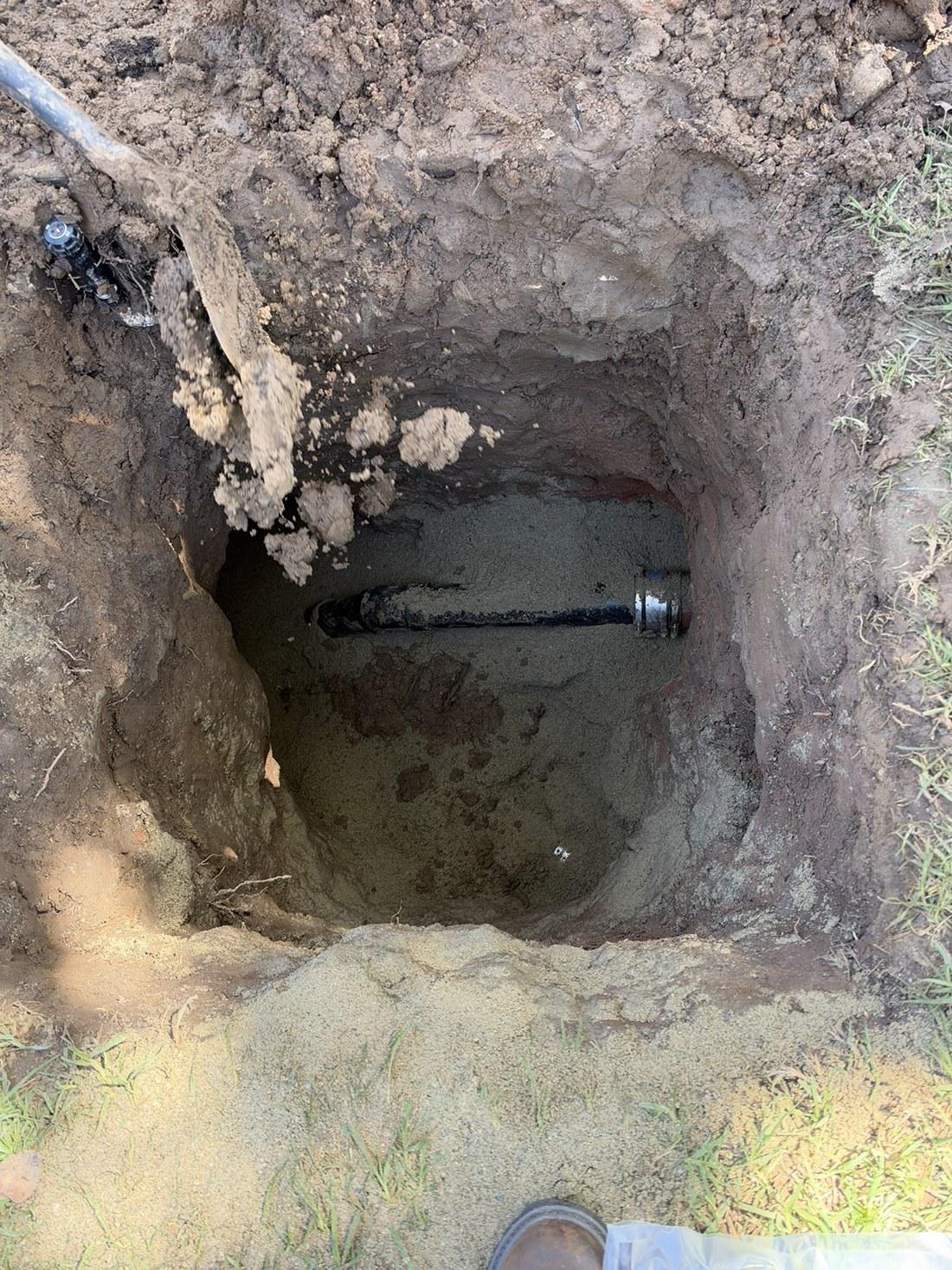 Excavated pit exposing buried cast iron pipe with bell joint