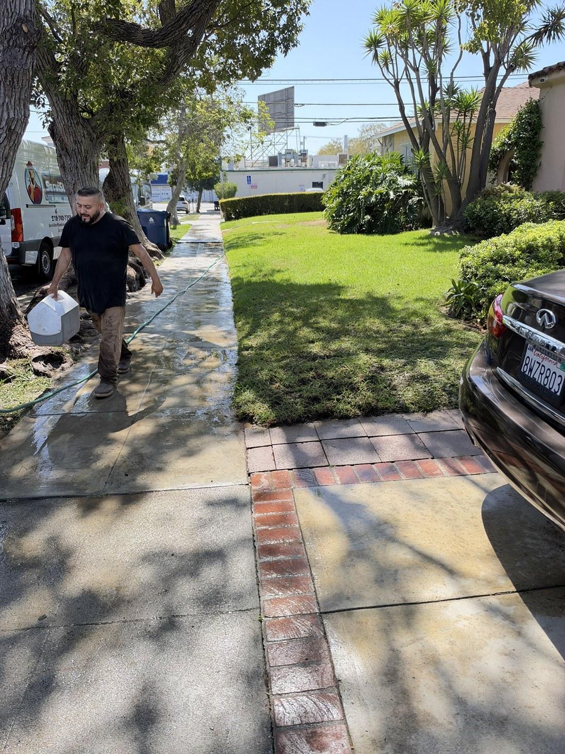 technician pulling garden hose on wet sidewalk near lawn