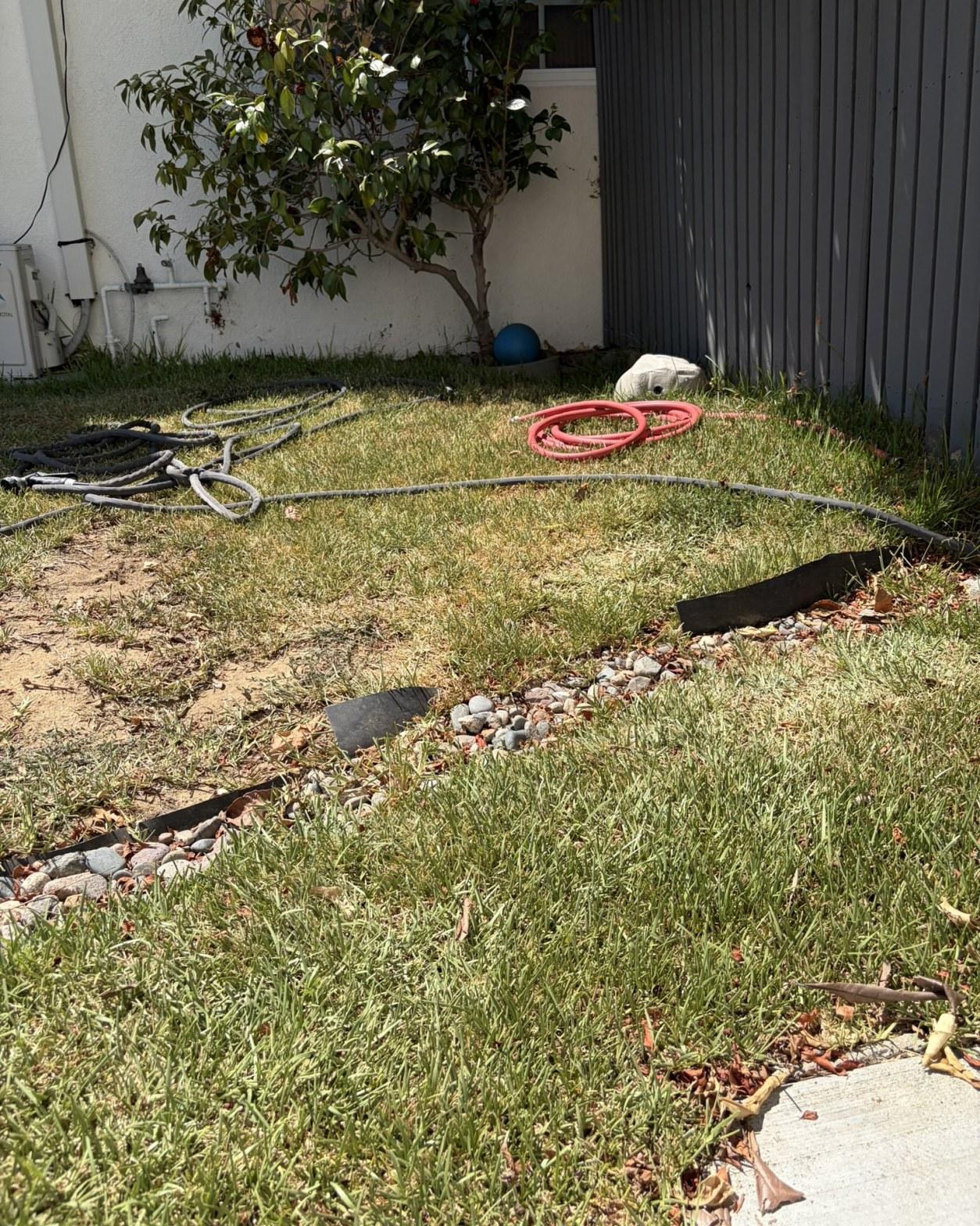 Old HVAC lines and hoses removed and staged on backyard lawn during residential systems renovation