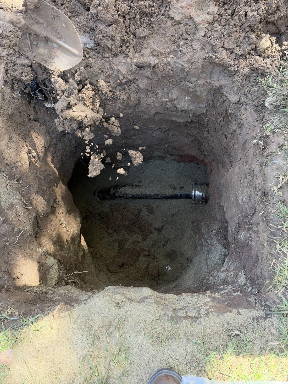 excavated pit exposing buried black cast iron sewer pipe