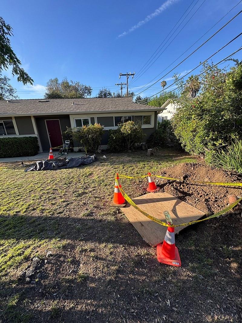 excavated trench with safety cones and caution tape in front yard